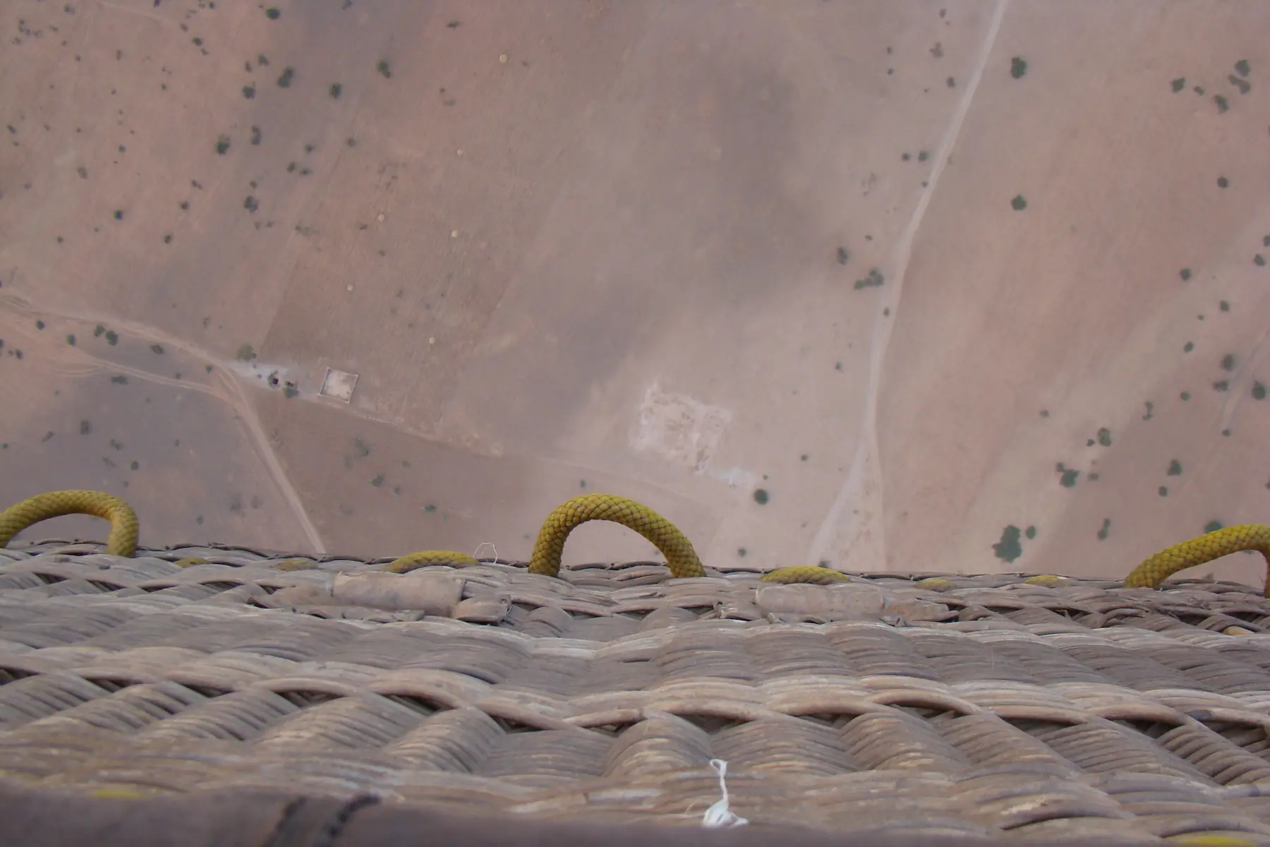 Arid plain with tracks and scattered shrubs seen from the edge of a balloon basket