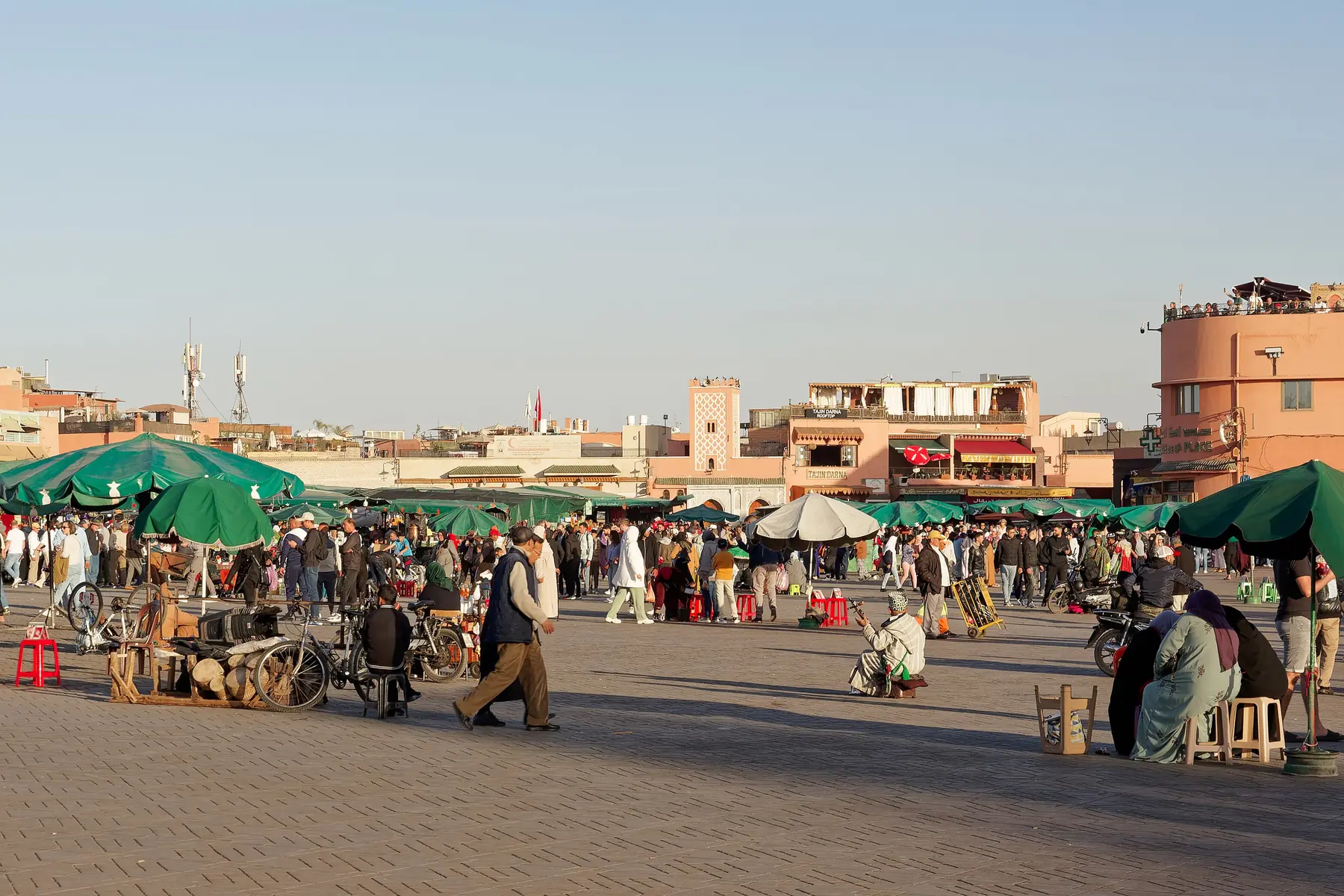 Jemaa el-Fna square with green parasols, stalls and people walking in the afternoon